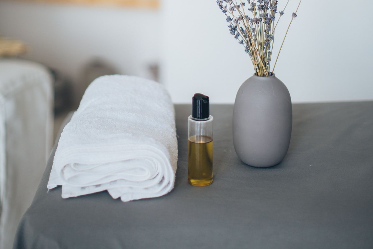 A folded towel, a bottle of oil, and dried lavender on a treatment bed
