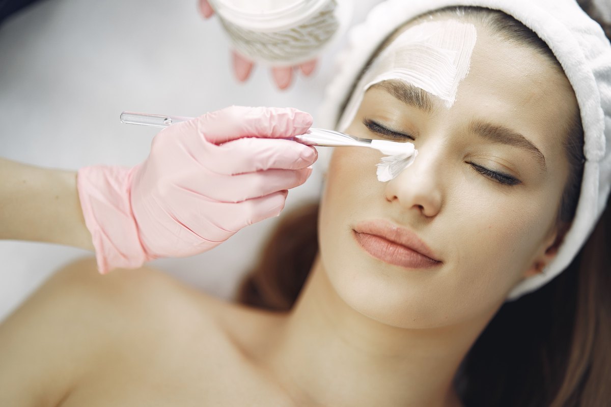 A gloved esthetician brushing peel solution onto a client’s face