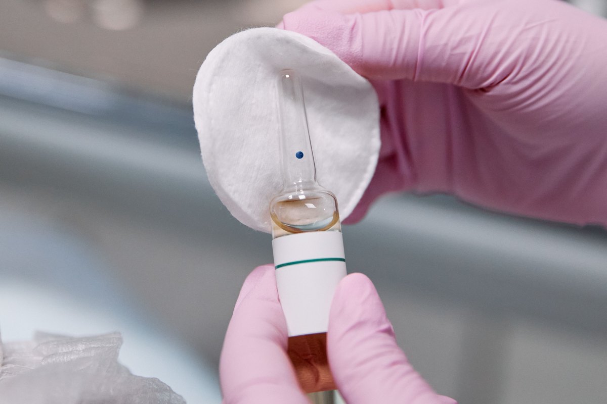 A gloved esthetician opening a single-use ampoule of peel solution onto a cotton pad