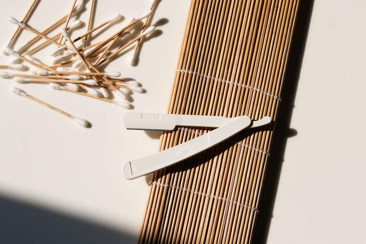 A dermaplaning blade and cotton buds laid out on a bamboo mat