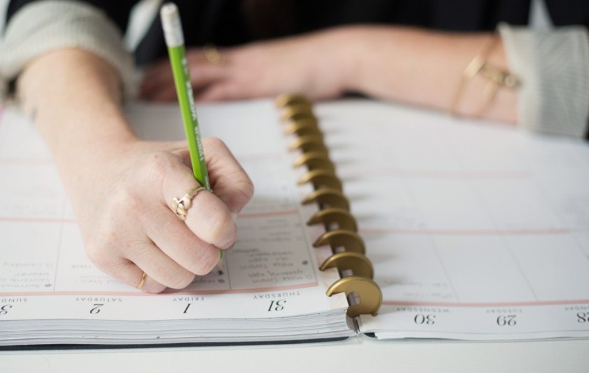 A hand writing in a notebook, planning a skincare schedule