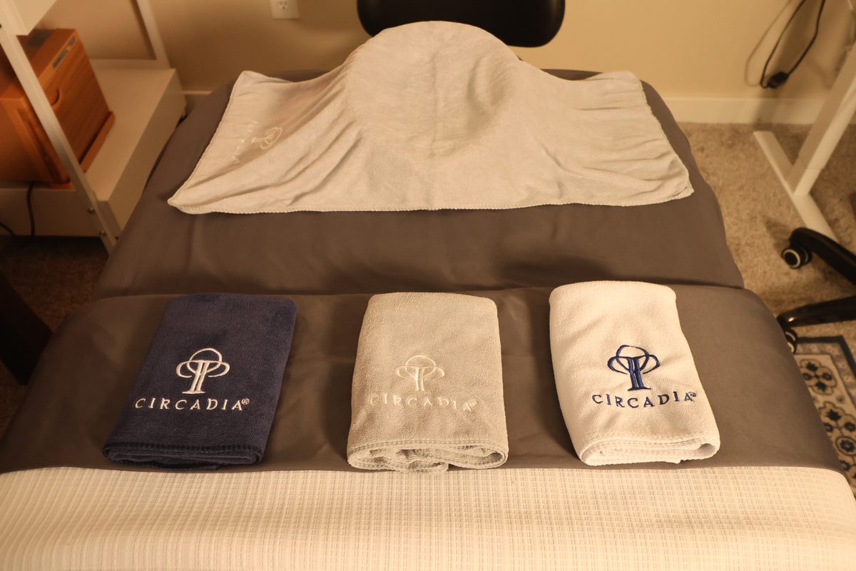 A facial bed in the treatment room at The Quiet Skin, made up with a gray blanket, a folded white towel at the head and three Circadia towels laid across the middle