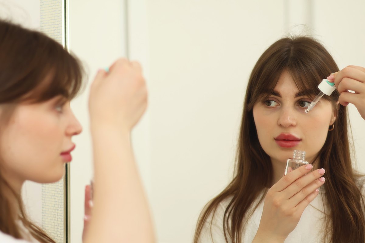 A woman applying post-peel serum with a dropper at the mirror